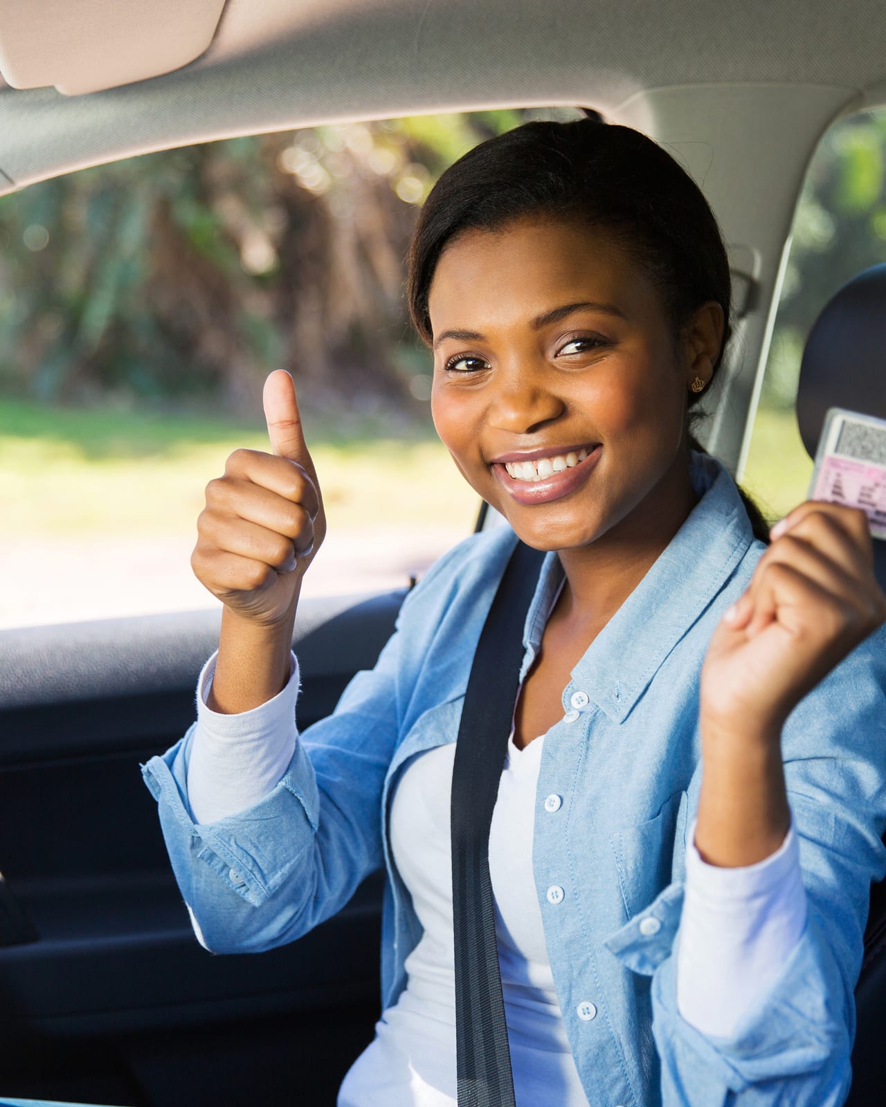 A QuickLyft Founding Driver smiling, holding her valid Ghana driver's licence inside her car
