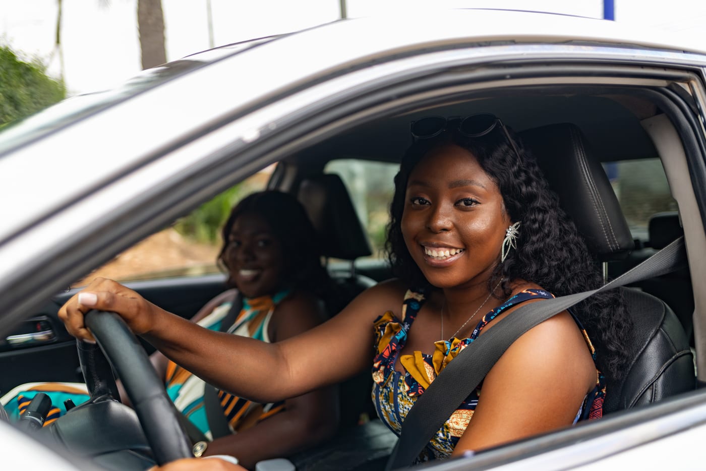 Two women in a verified private car &mdash; driver and passenger with seatbelts on &mdash; illustrating QuickLyft Women-Only mode